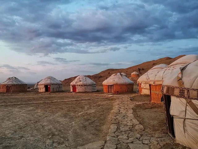 A group of traditional yurts set up in a desert landscape under a cloudy sky.