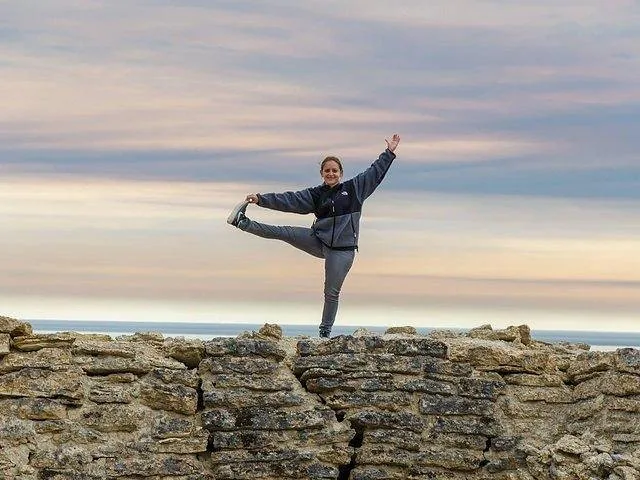 Woman standing on one leg on a stone wall overlooking water