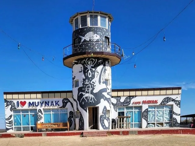 A lighthouse-shaped cafe building with murals in Muynak, under a blue sky.