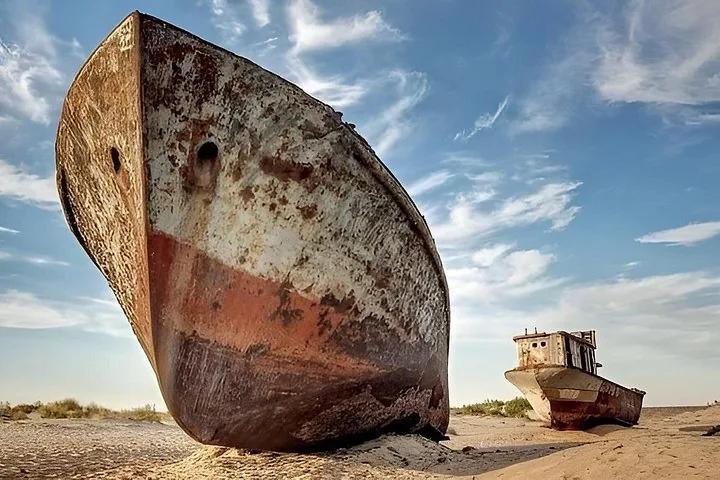 Two large, rusted ships resting on the sandy bottom of the dried Aral Sea.