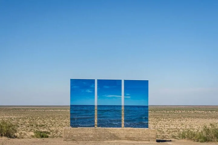 Three blue glass panels standing in a desert landscape reflecting the sky