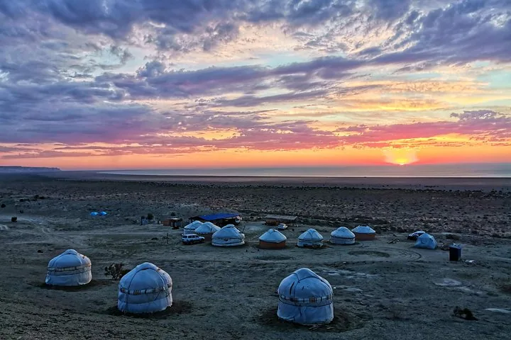 Yurt camp in a dry landscape with the Aral Sea visible under a vivid sunset.
